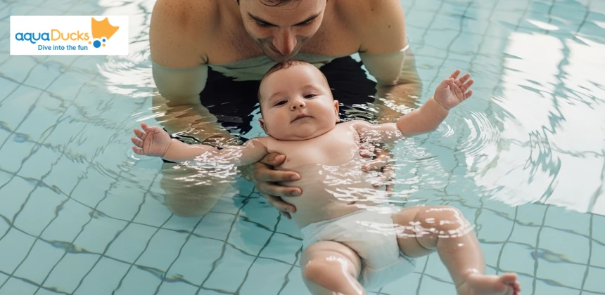 A father supporting a 5-month-old baby in a back-float position during a gentle swimming lesson, showing the best age to start swimming lessons for infant in a calm indoor pool 