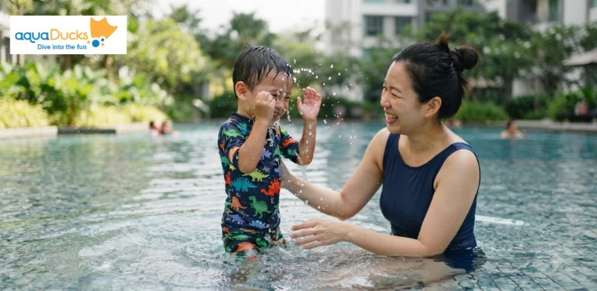 A young child laughing and splashing water in a pool with their parent to build confidence and feel safe while learning to swim