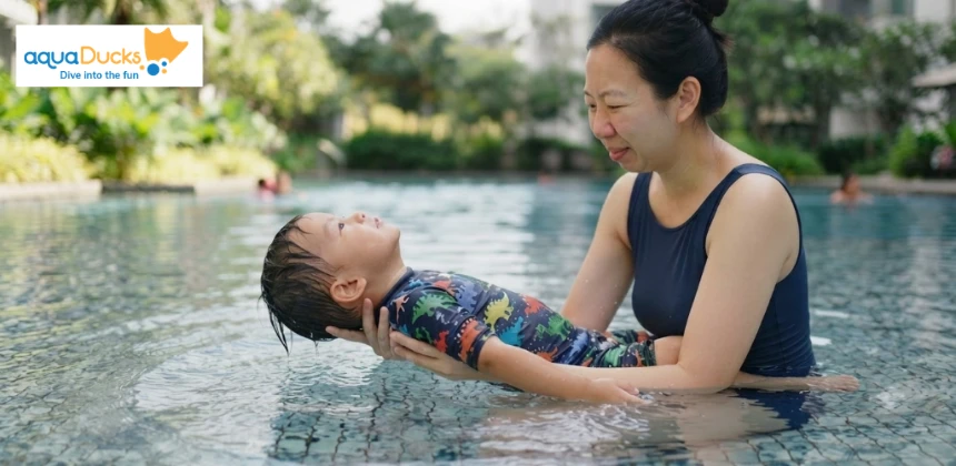 A parent gently supports their young child in a back float position in a swimming pool, teaching them to stay calm and float.