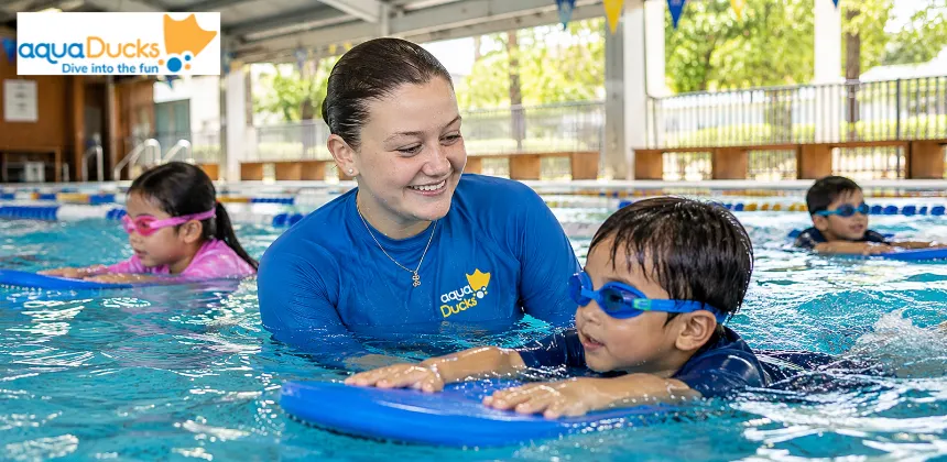 AquaDucks swimming instructor watching a child practise swimming with a kickboard