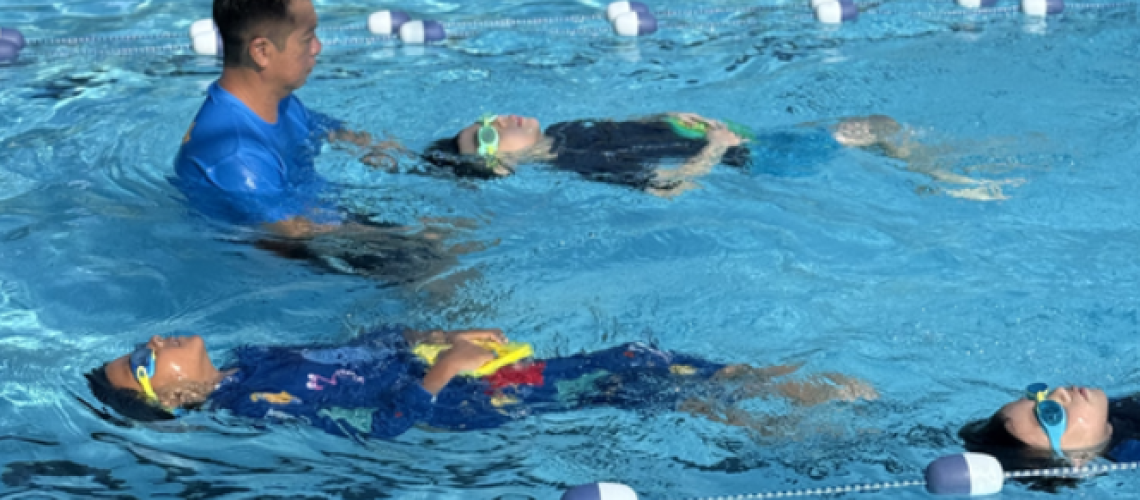 A pool instructor and three children enjoy swimming lessons together in a pool aquaDucks