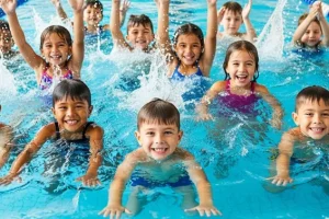 A diverse group of young children happily participating in a guided swimming lesson in an indoor pool.