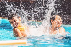 Two boys at the swimming pool splashing water and having fun. Friends playing on the water of a summer day.